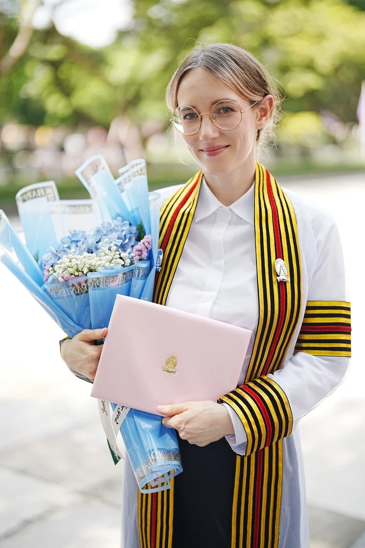 Alja Grofelnik Pelzel outdoors, holding flowers on her graduation day.